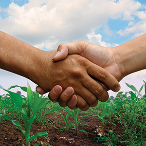 A handshake happens in a farm background.
