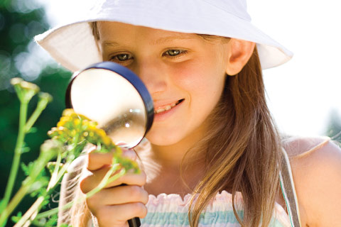 Girl inspecting plant with magnifying glass